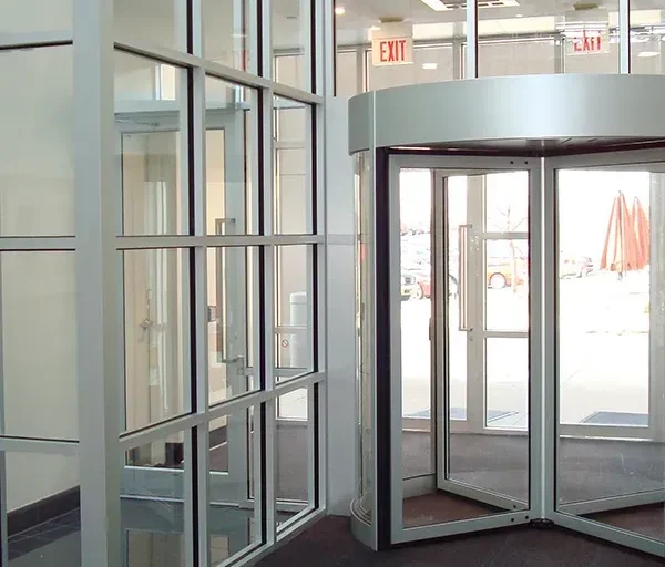 Modern glass entrance with a revolving door and exit signs.