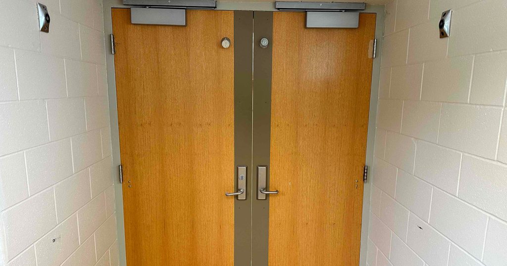Industrial door installation showing a pair of wooden doors with hardware being retrofitted for code